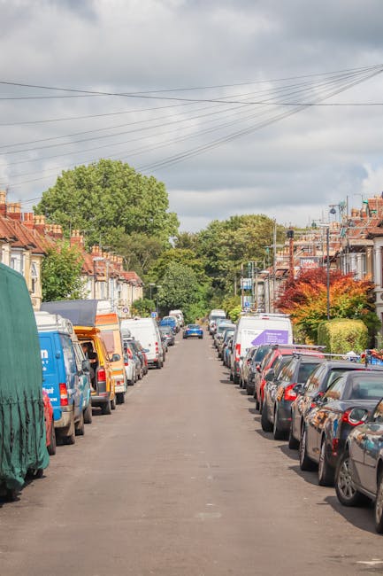A narrow cobbled street in Ickenham, lined with red brick terrace houses featuring white-framed windows and doors. On the left, a person is working on packaging or wrapping household items, with some