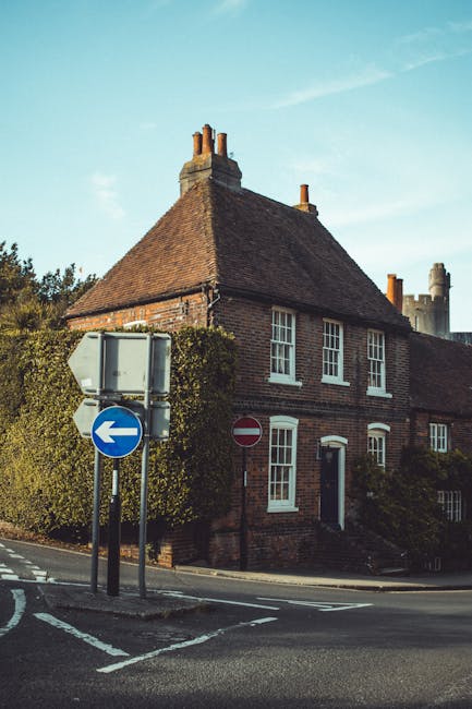 Exterior view of a traditional half-timbered house with white walls and dark wooden beams, situated behind a small garden with green shrubs, flowering plants, and climbing vines along the facade. The